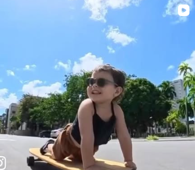 Criança sorrindo deitada de barriga no longboard